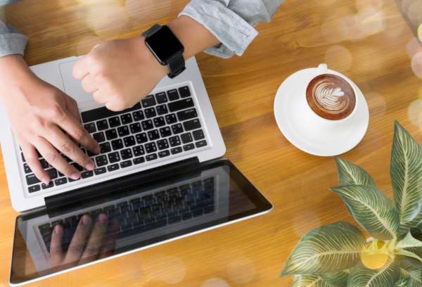 hands typing on laptop computer with coffee on wooden table